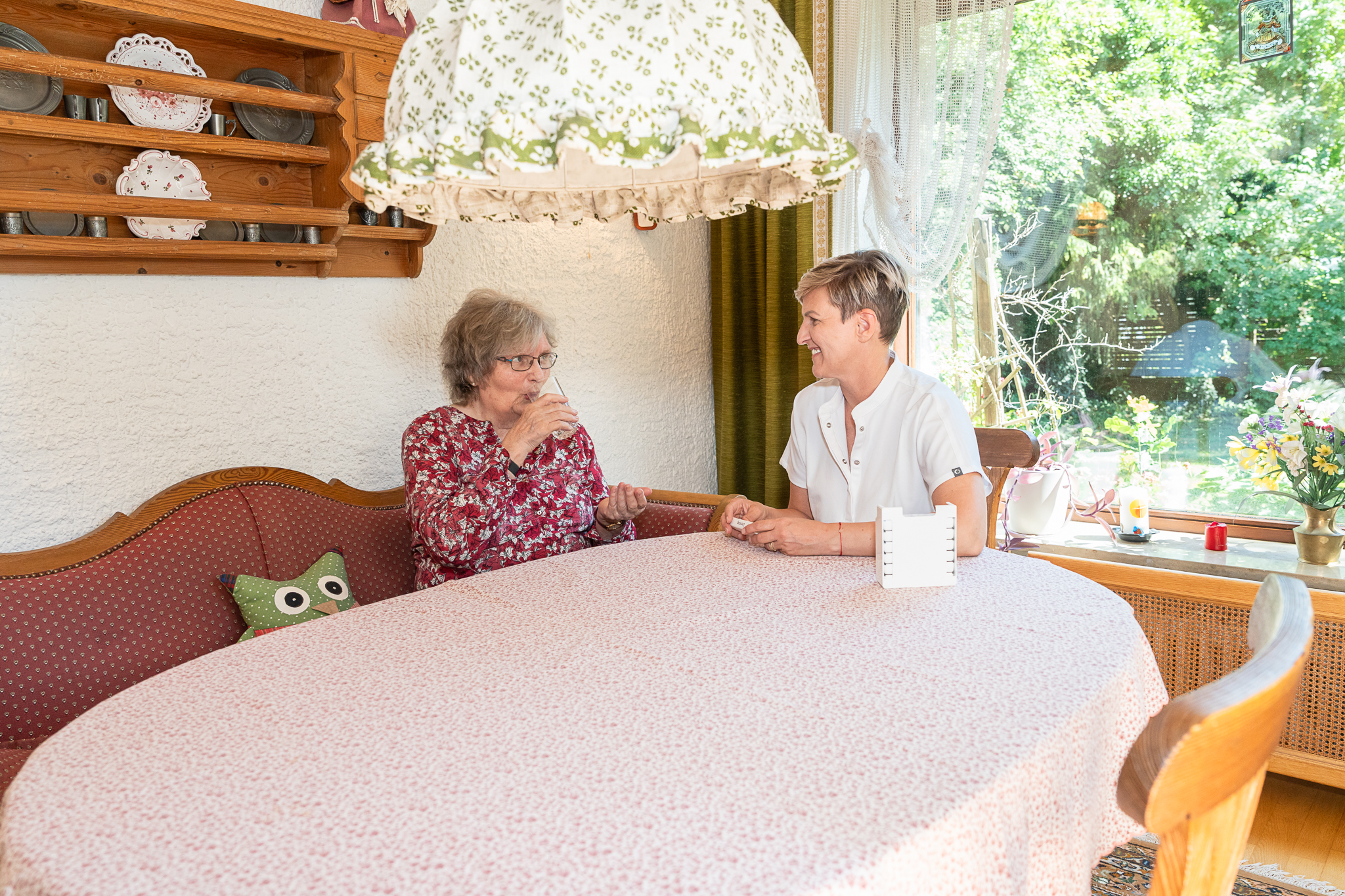 Gespräch zwischen Pflegekraft und Seniorin am Esstisch am Fenster