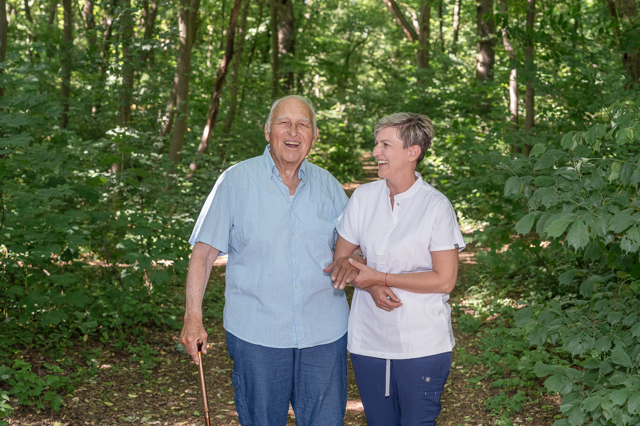 Pflegekraft begleitet Senior bei einem Spaziergang im Grünen