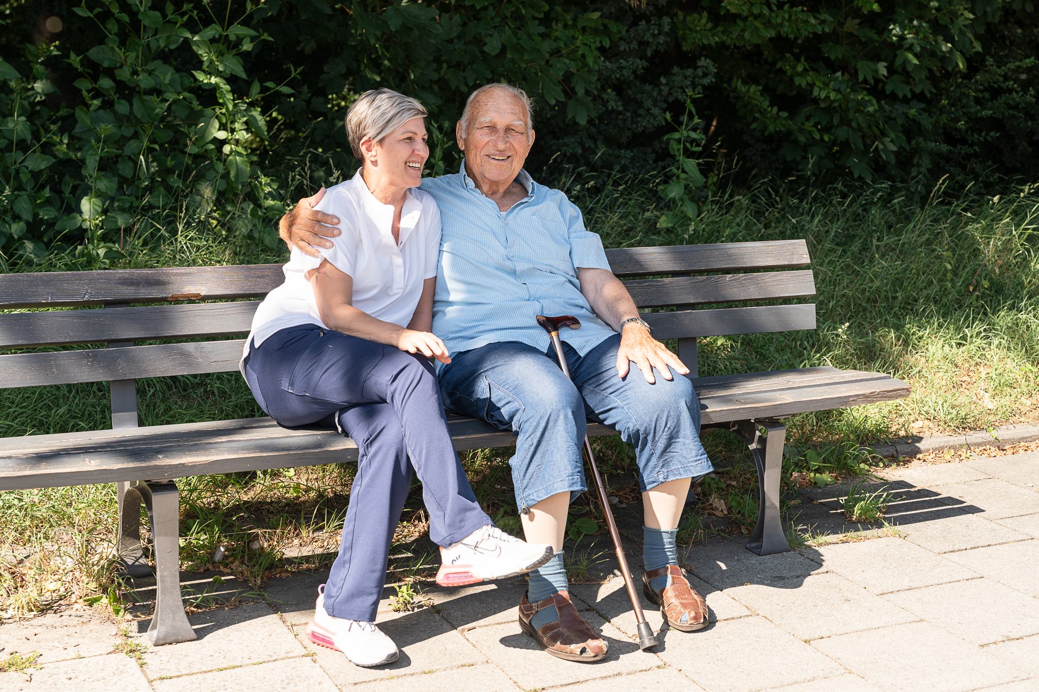Pflegekraft sitzt mit Senior auf einer Parkbank