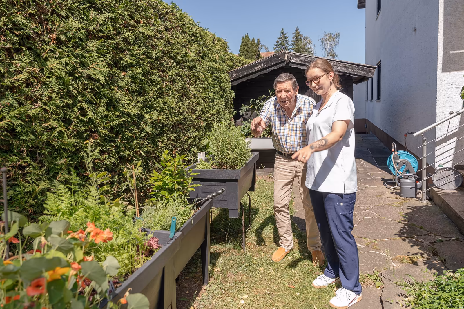 Zwei Pflegekräfte helfen einem Senior beim Gehen im Garten