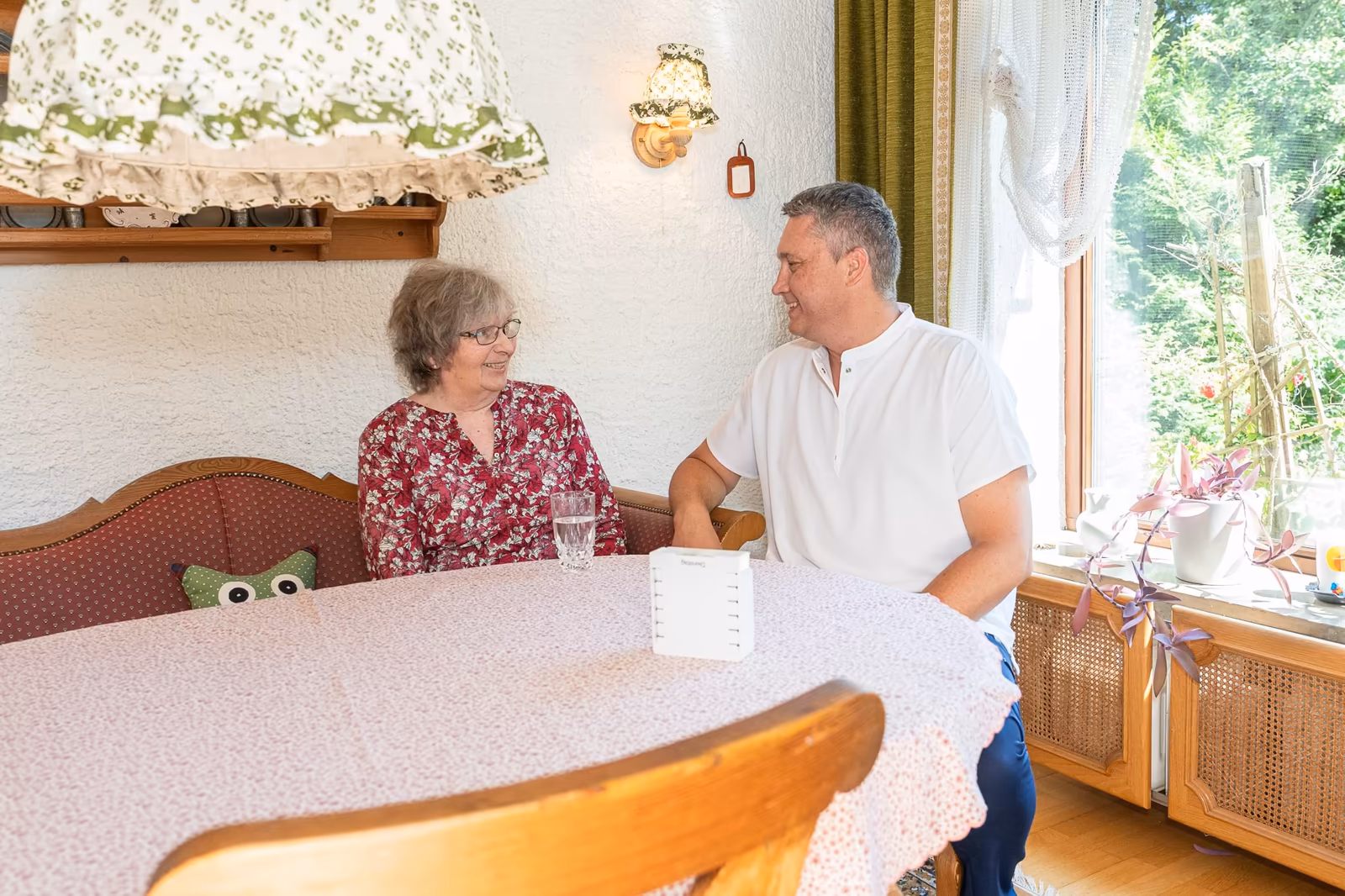 Pflegekraft und Senior im Gespräch bei Kaffee am Esstisch